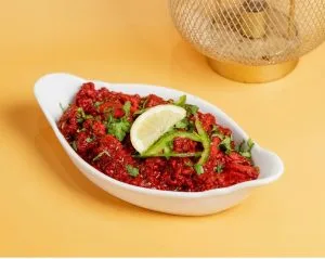 Red spiced dish with coriander and a lime wedge in a white bowl