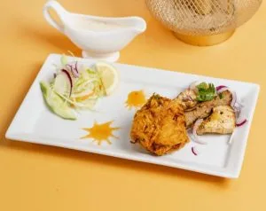 Grilled pieces on a white plate with salad and a small jug of sauce